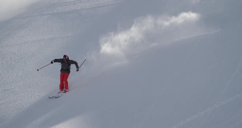 A skier sends up clouds of snow as they descend a snowy mountain slope on a sunny day