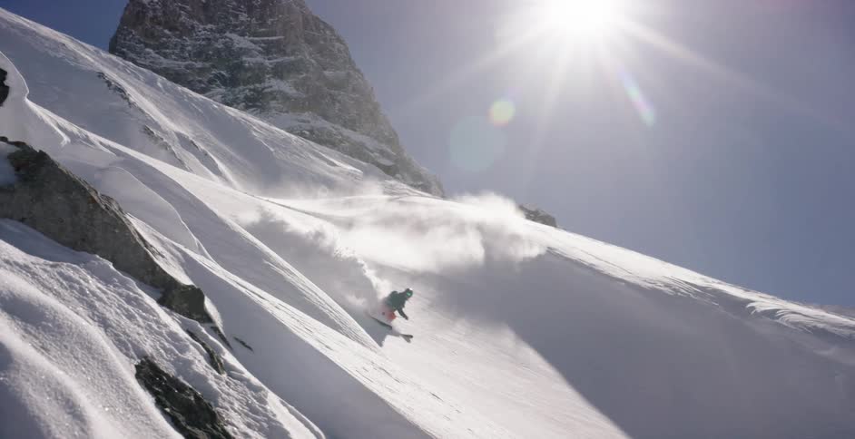 A person skiing down a snowy mountain as the sun shines