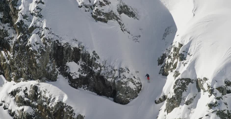 Skier skis down snow covered mountain in and out of shadows