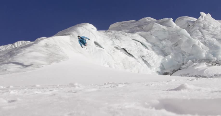 A skier does multiple twists in the air as he jumps while making a turn on a mountain