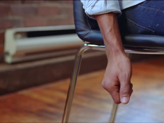 A person sitting on a chair in a room closes hand into a relaxed fist