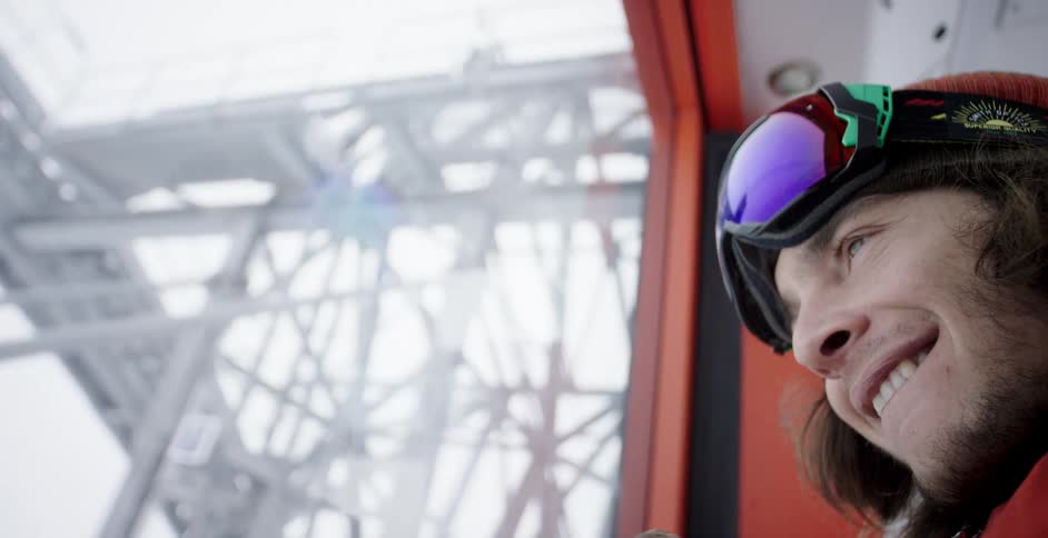 A man with a hat goggles and gloves looking out a window and smiling