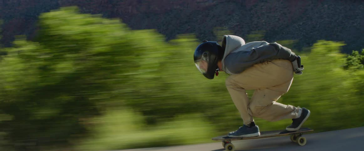 A skateboarder speeding down a rural paved road in summer