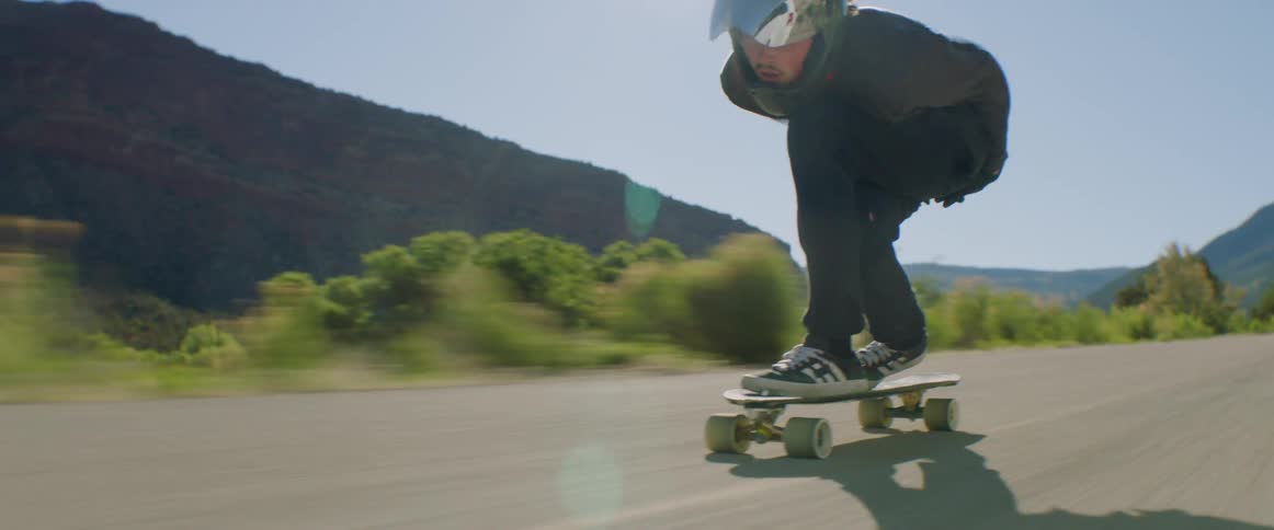 A person with a helmet and gloves riding on a road on a skateboard