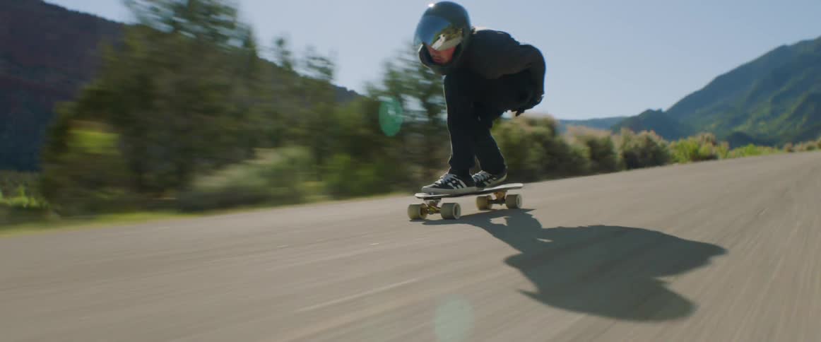 Skateboarder with a helmet rides a skateboard at high speed on a country road with mountains in the background