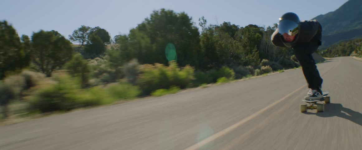 Young man wearing a crash helmet rides a skateboard at full speed down a road on the badlands