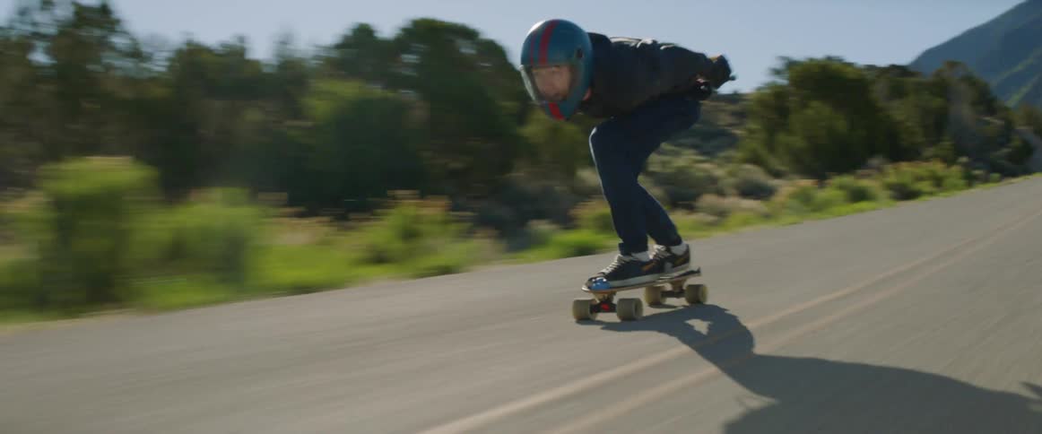 Person skateboards along highway past mountains and scrub on clear day