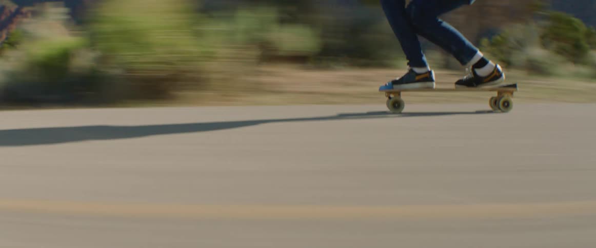 Person skateboards along highway past scrub and mountains