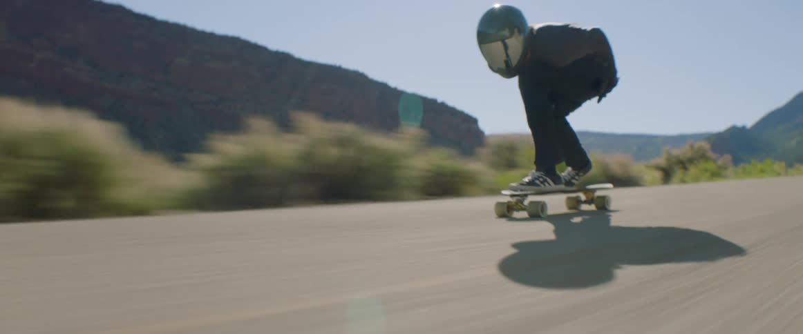 A person with a helmet and gloves skating down a road on a skateboard
