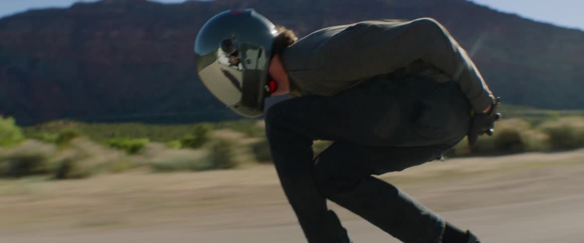 Young man wearing a crash helmet rides a skateboard down a road at full speed on the badlands