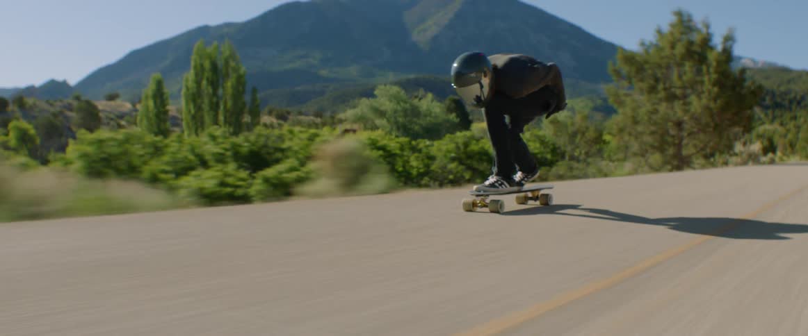 Skateboarder with a helmet rides a skateboard at high speed on a country road with mountains in the background