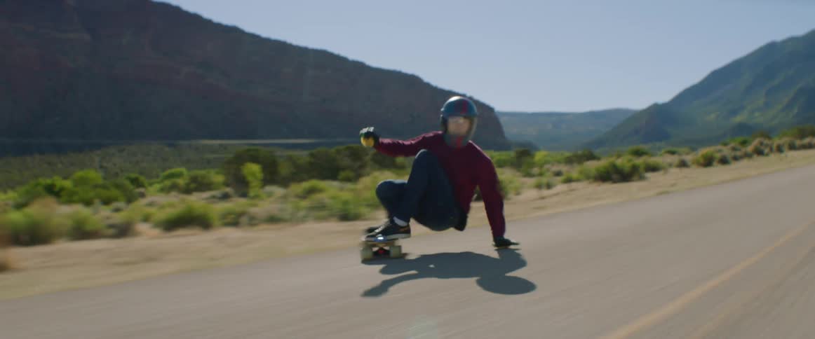 People skate along highway past mountains performing tricks
