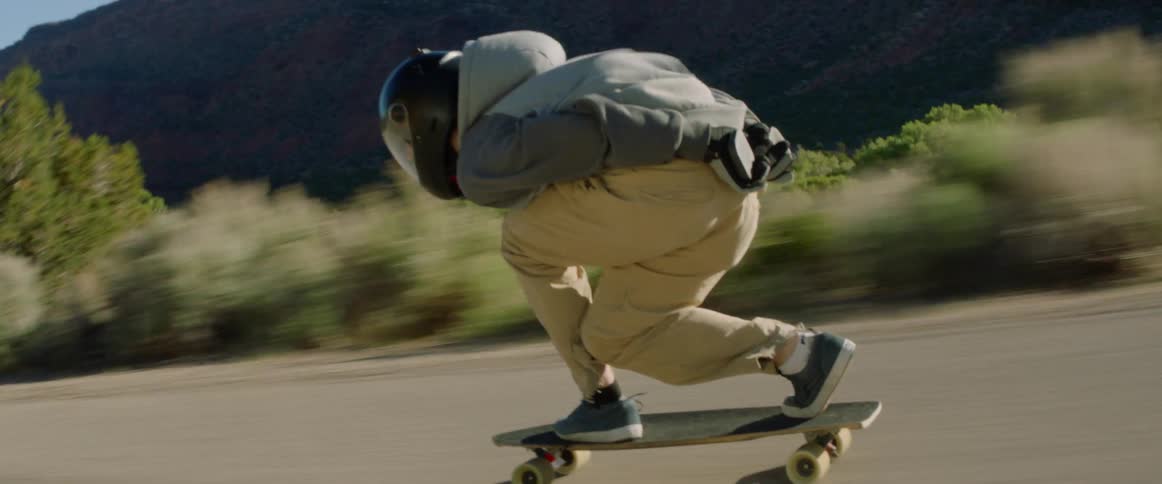 A skateboarder speeding down a paved road in mountains on a sunny day