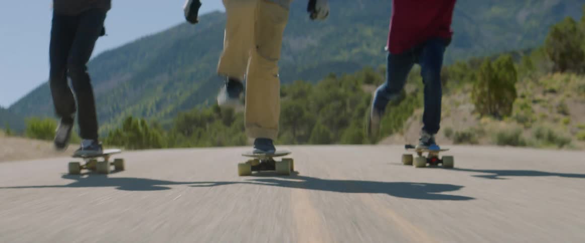 Three teenage boys riding skateboards on rural highway in front of mountain
