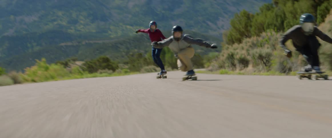 Group of friends wearing crash helmets and protective gloves ride skateboards downhill at full speed