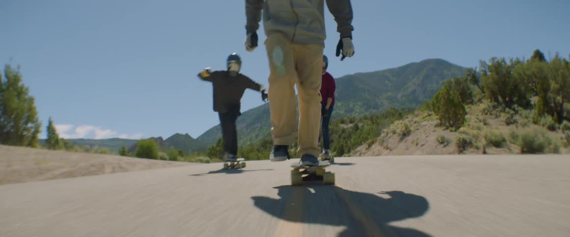 Group of friends wearing crash helmets and protective gloves skateboard full speed downhill