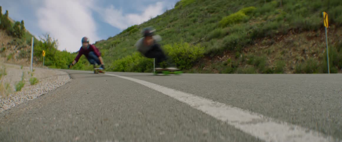 People with helmet and gloves skateboarding down a road