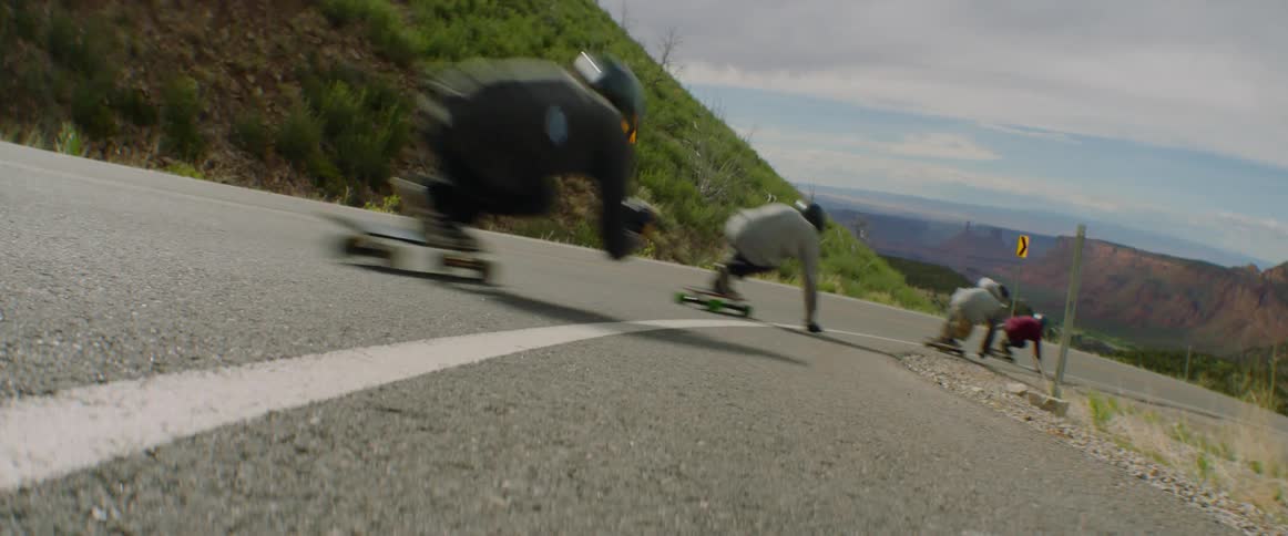 A group of people skateboard on a quiet rural road