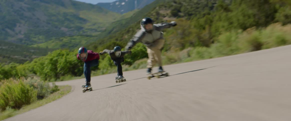 Three teenagers race on skateboards down a street