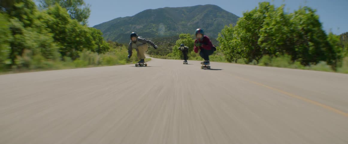People with helmet and gloves skateboarding down a road