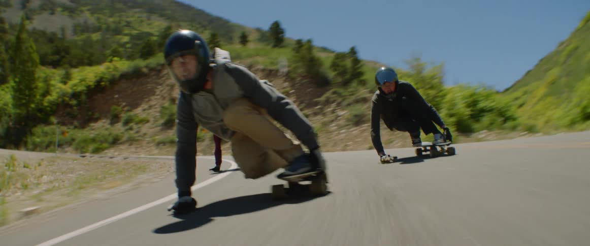 Skateboarders ride downhill on a winding road at high speed in the mountains
