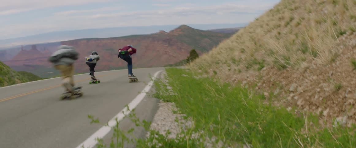 Three skateboarders ride skateboards downhill at high speed