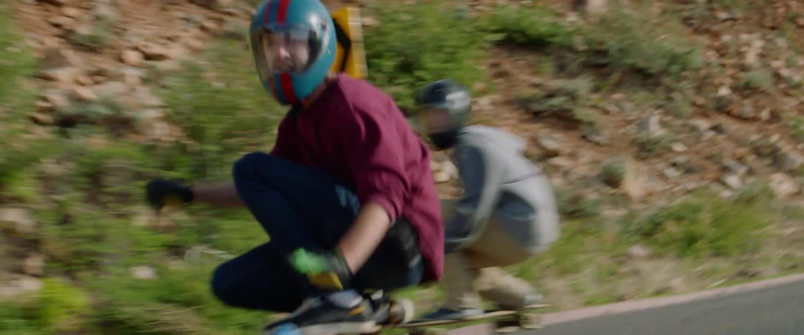Skateboarders on highway crouch to take curve on hill