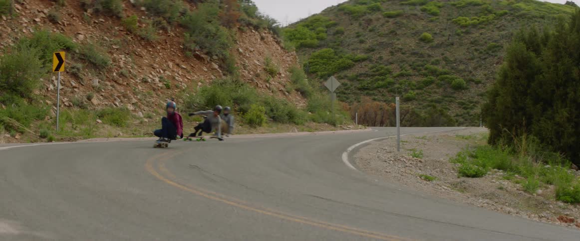 Skateboarders speeding down a rural hillside on a summer day