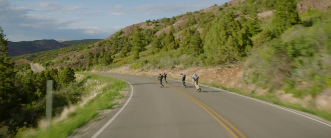 Three people skateboard on a rural hillside road