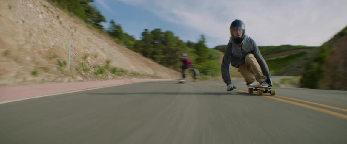 Skateboarders ride downhill on a winding road at high speed
