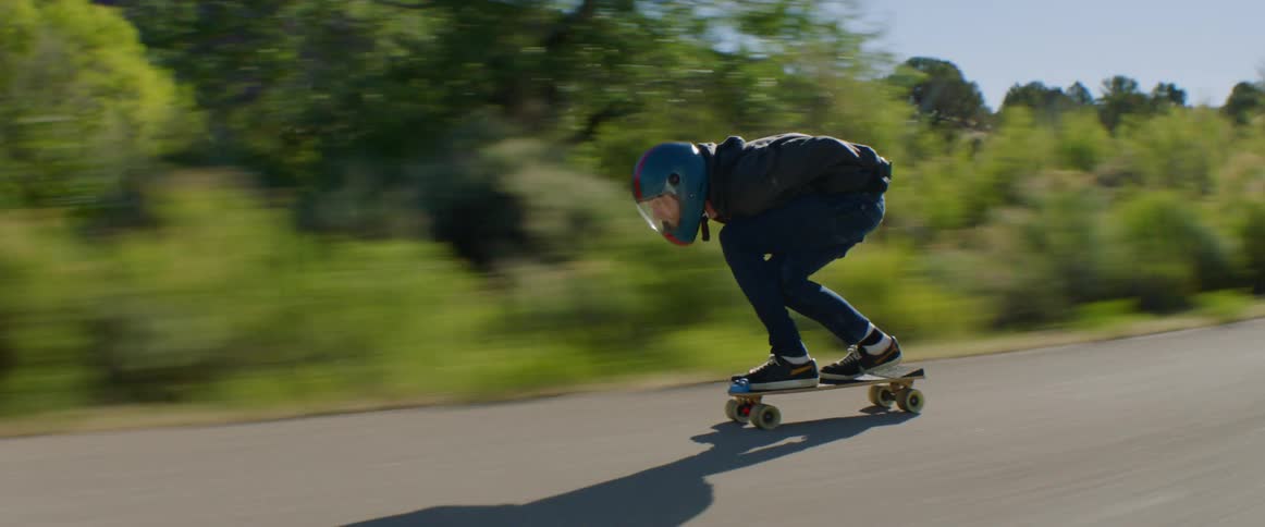 A person with helmet and gloves skateboarding down a road