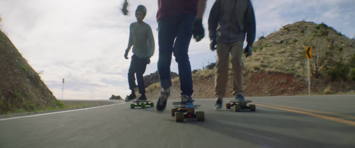 Three people ride skateboards on a quiet rural road