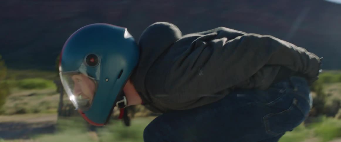 A skateboarder hunches over for aerodynamics while skating down a road through the badlands at high speed during the day