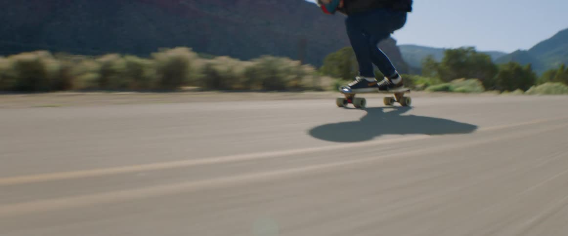 Male skateboarder rides downhill on a winding road at high speed