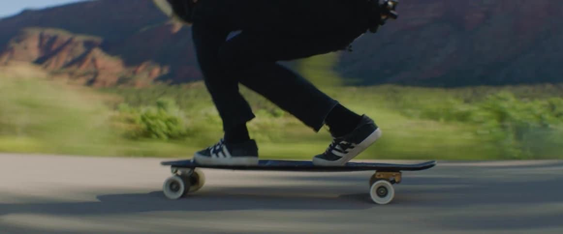 Person rides skateboard along highway passing scrub and mountains