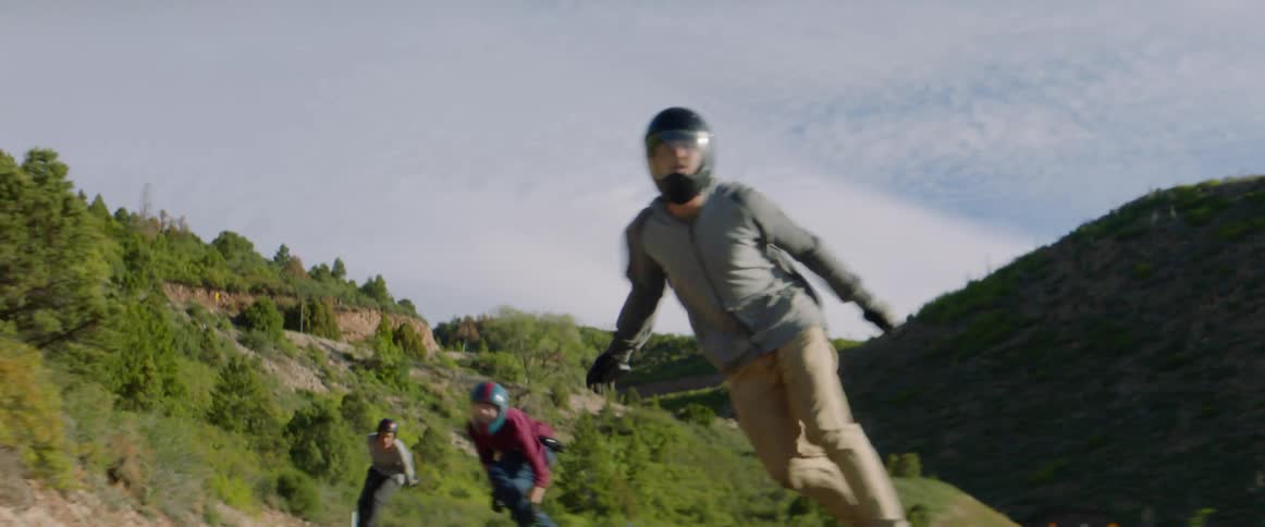 Three people skateboard down a hillside road