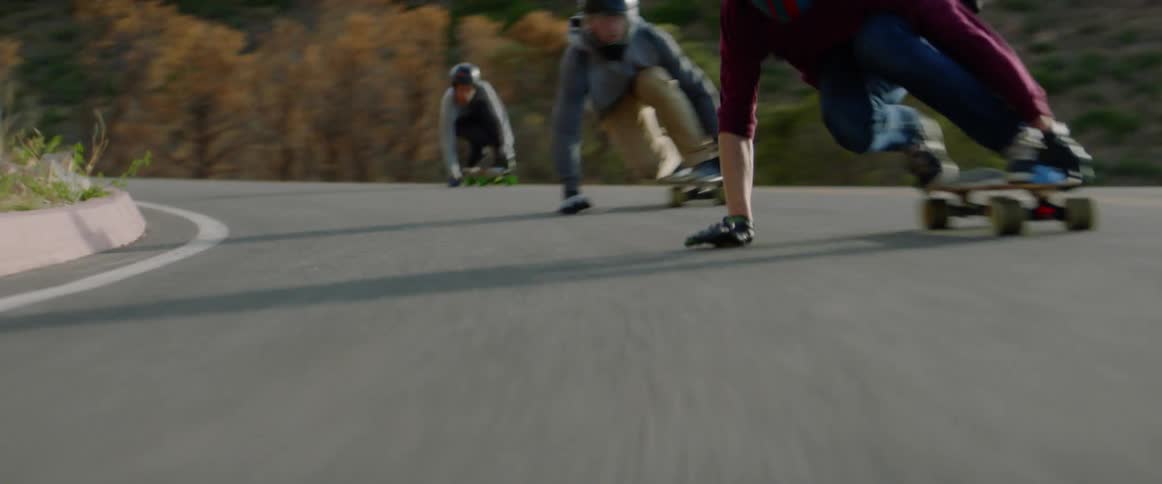 Three males skateboarding down a hilly road