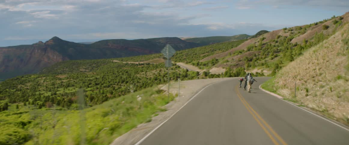Skateboarders speeding down a rural hill on a summer day