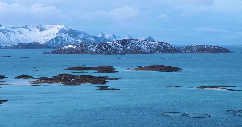 Small islands and fish farms of the coast of a snow capped mountain during the day