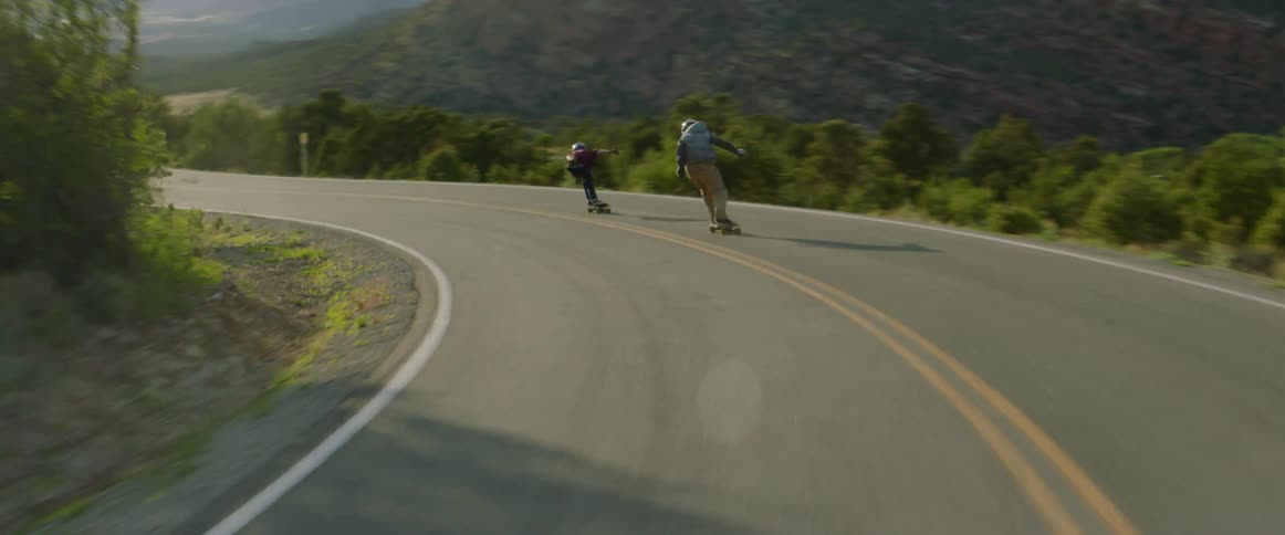 Skateboarders ride downhill on a winding road at high speed