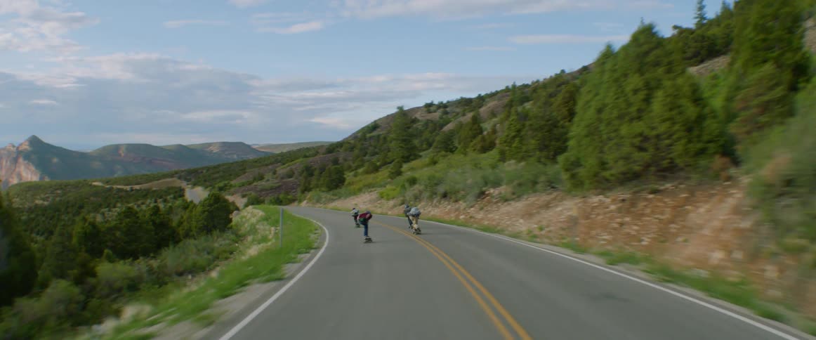 People with helmet and gloves skating down a road on skateboards