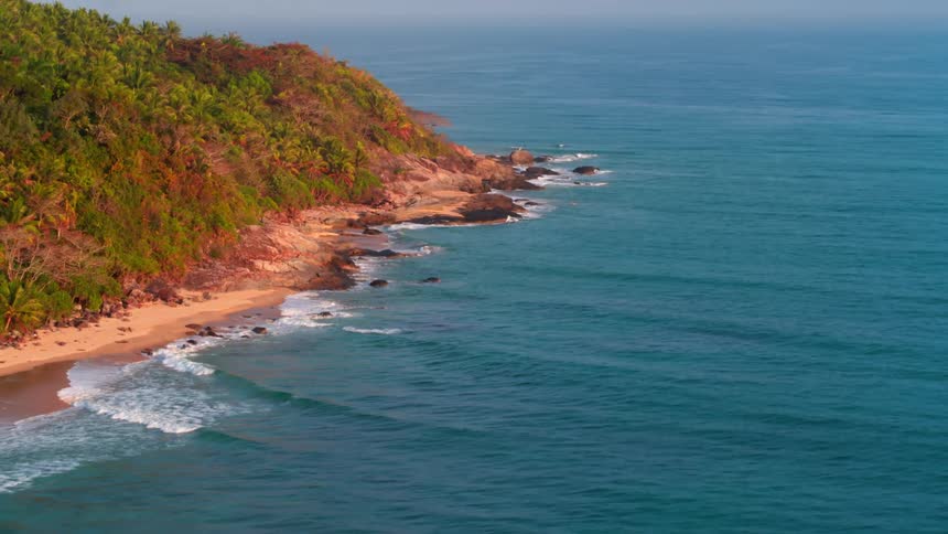 Waves crash against shore backed by forest covered mountains