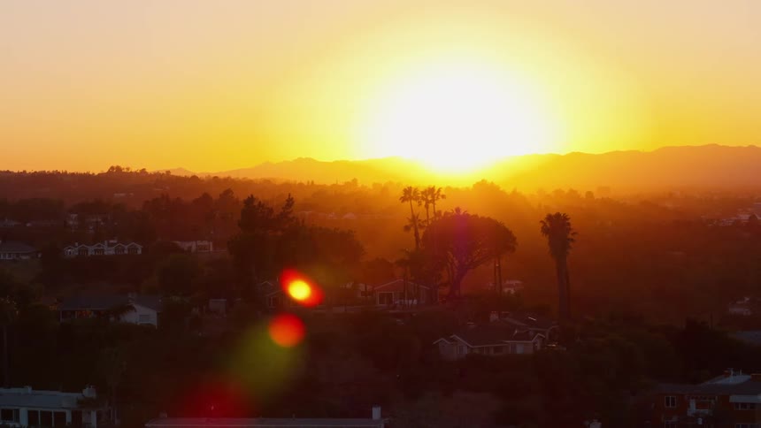 The sun setting over buildings and trees in a neighborhood