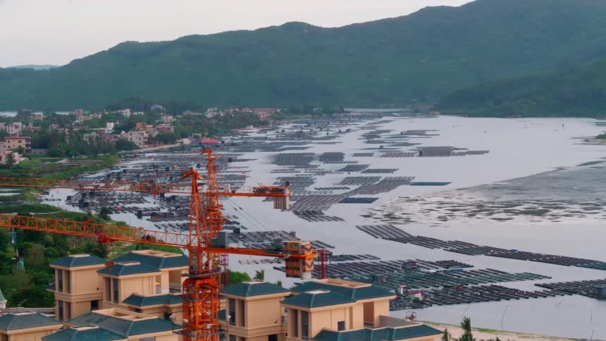 A coastal city with buildings and trees with a mountain range the sky and clouds in the background