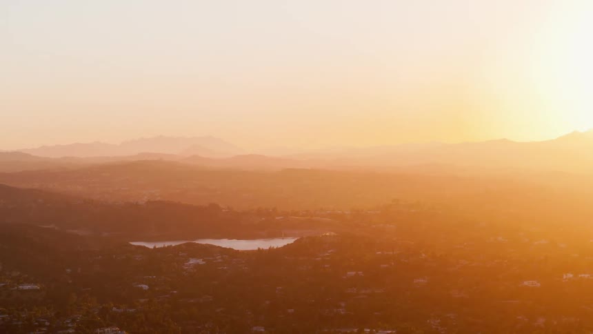 The sun setting over a distant mountain with a lake in the foreground
