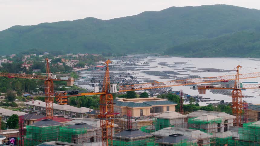Mist cover mountain on horizon as construction cranes and scaffolding stand around houses near water
