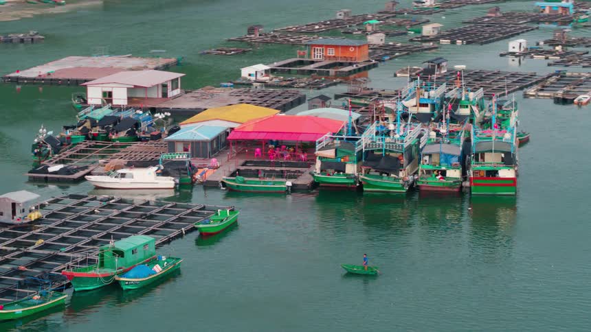Aerial view of green fishing boats next to floating fish farm in the calm green waters next to the coast