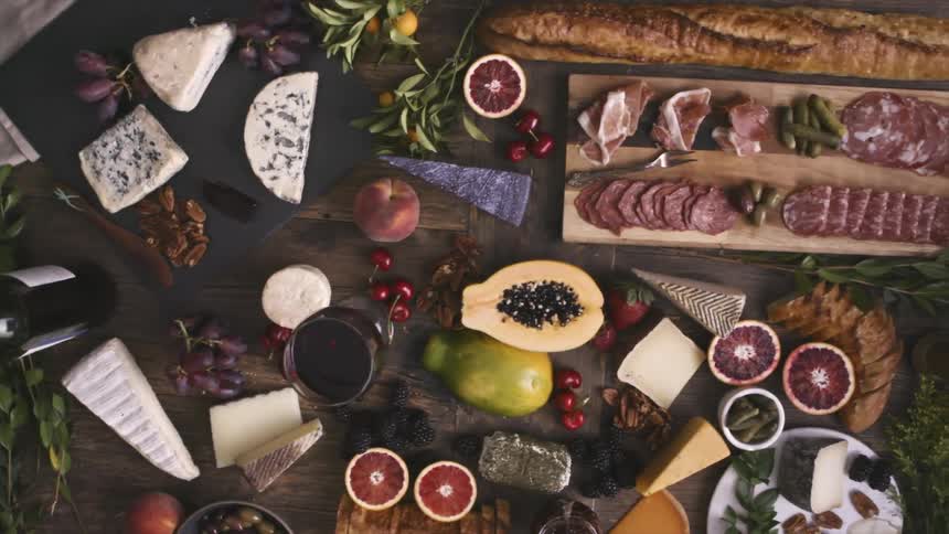 A hand is arranging different types of food over a wooden table