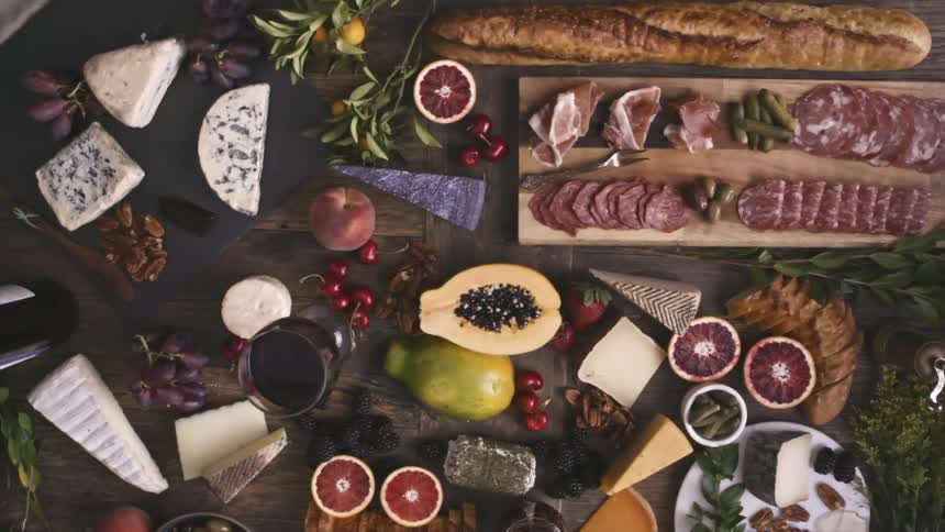 A hand places a cherry on a wooden table covered in food and wine