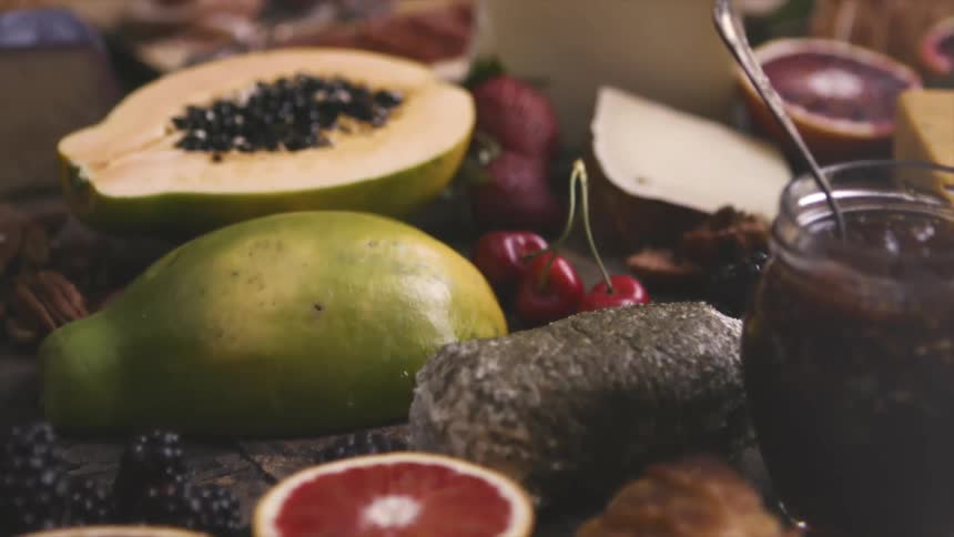 A wide variety of fruits plus bread and cheese fill the surface of a wooden table